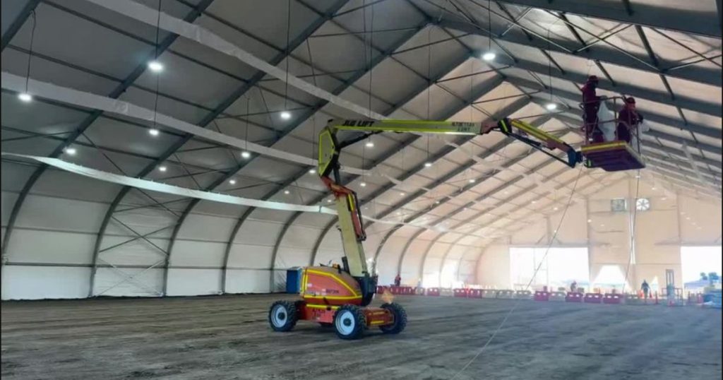 Montaje interior de una carpa modular de gran tamaño con brazo hidráulico y operarios trabajando en altura.